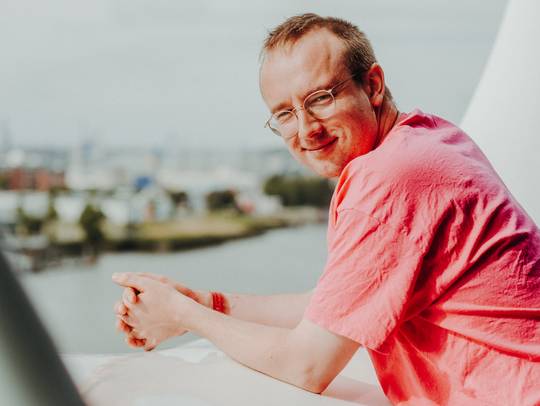 Porträt von Alex Paxton, auf dem Geländer der Elbphilharmonie-Plaza lehnend