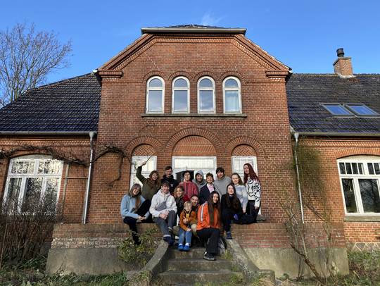 Die Stipendiat:innengruppe steht bei ihrer Jahrgangs-Residenz 2024 stART.up auf Falster vor der Unterkunft im Sonnenschein