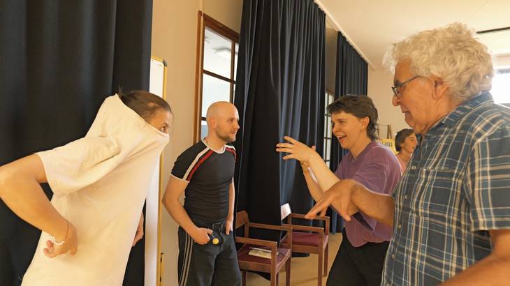 Foto von vier Personen beim Theaterworkshop. Eine Zeigt mit dem Finger auf eine Person, die den Kopf in ihr T-Shirt gezogen hat.