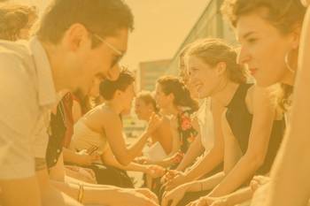 Bild mit jungen Menschen, die sich gegenüber sitzen und angeregt austauschen, draußen, Foto mit gelbem Overlay und Text Kunst & Kultur