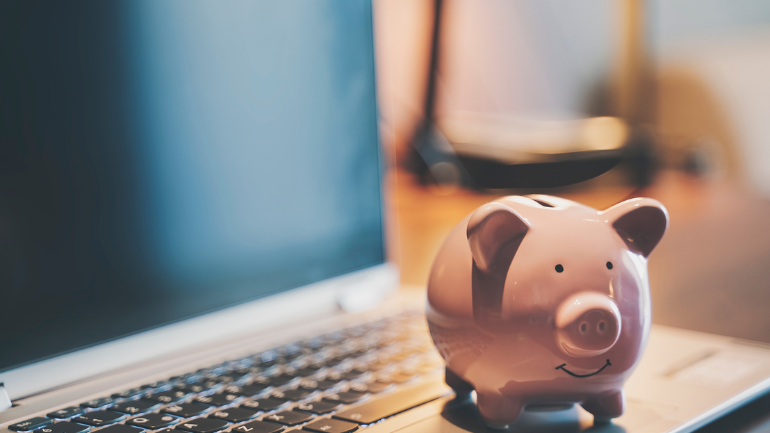 Ein rosa Spar-Schwein steht auf der Tastatur eines Laptops